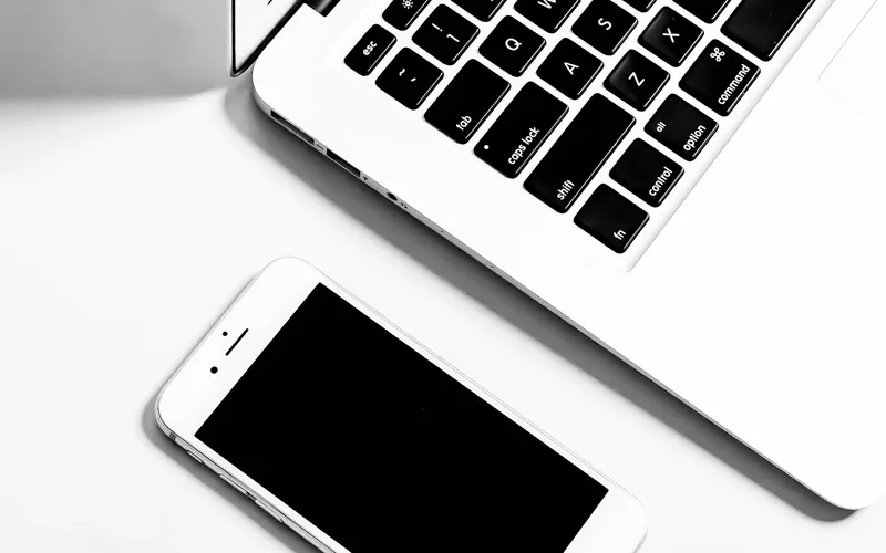 Computador portátil e celular sobre uma mesa.